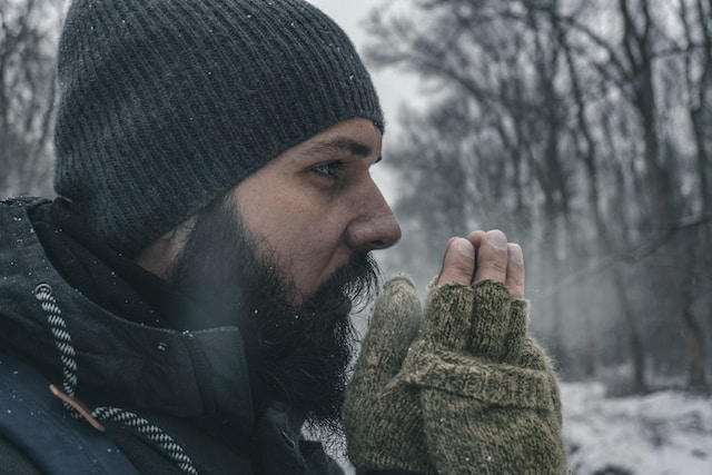 A close-up profile of a man in the woods wearing gloves